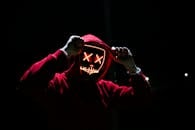 A spooky illuminated mask figure with a red hoodie in a dark setting, perfect for Halloween themes.